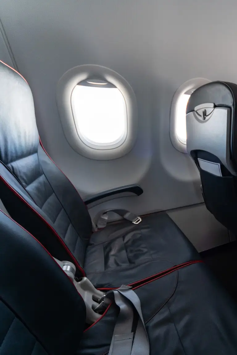 two dark seats with red edges and seat belts next to a window in quiet airplane