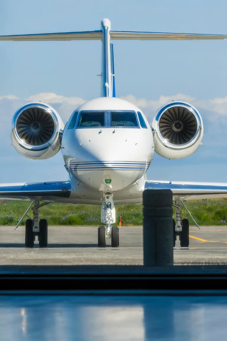 a white private jet with blue accents and two large engines on a tarmac under a clear sky