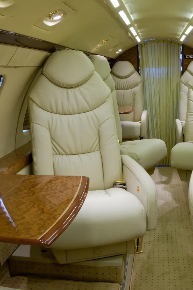 the interior of a luxurious airplane with cream colored leather seats a wooden table and curtains