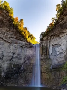 a breathtaking view of Taughannock Falls in Upstate New York, where crystal clear water cascades down a rugged cliff adorned with vibrant autumn foliage.