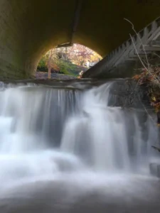 serene waterfall flowing under a corbett's glen with perimeter trail, surrounded by lush greenery